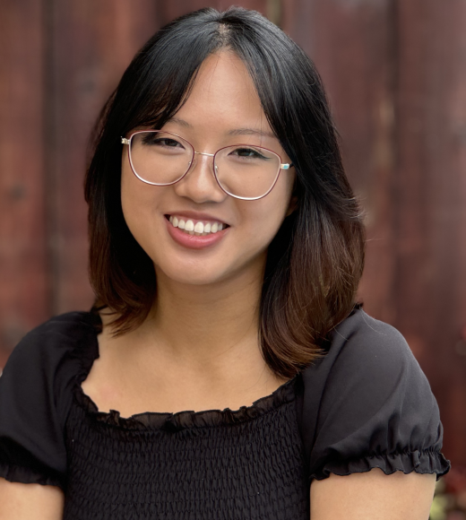 Andrea profile picture, wearing a black shirt and behind a wooden fence background