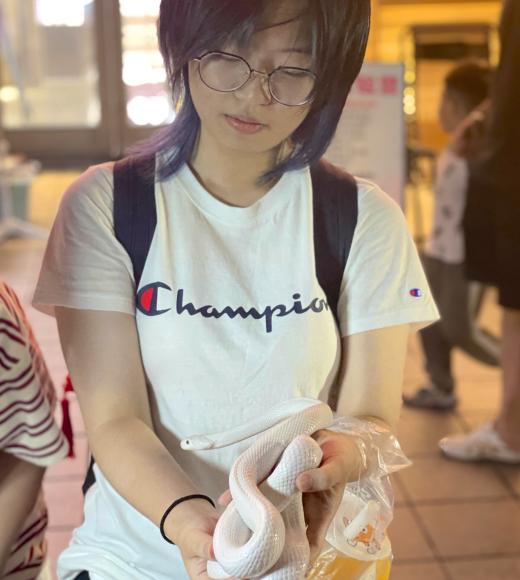 Photo of Carly wearing a white shirt with a black backpack holding a white snake