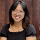 Andrea profile picture, wearing a black shirt and behind a wooden fence background