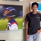 photo of Will wearing a black shirt and blue jeans standing next to a portrait of a baseball player